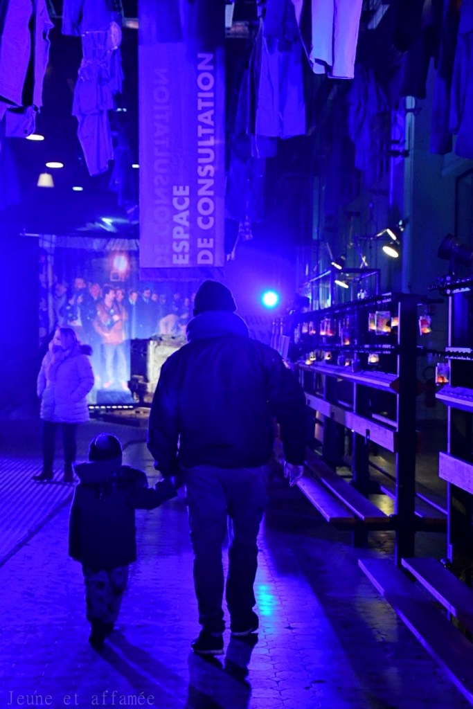 Un père et son fils de dos, se tenant la main dans la salle des pendus de la base du 9/9 bis