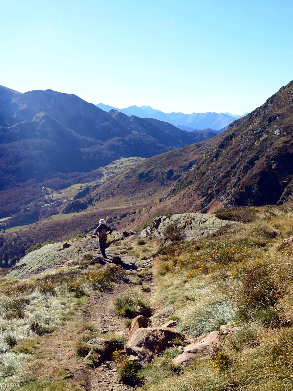 Chemin qui mène à l'étang d'Arbu. On voit de l'herbe au premier plan, quelqu'un marche sur le sentier, on voit des montagnes derrière