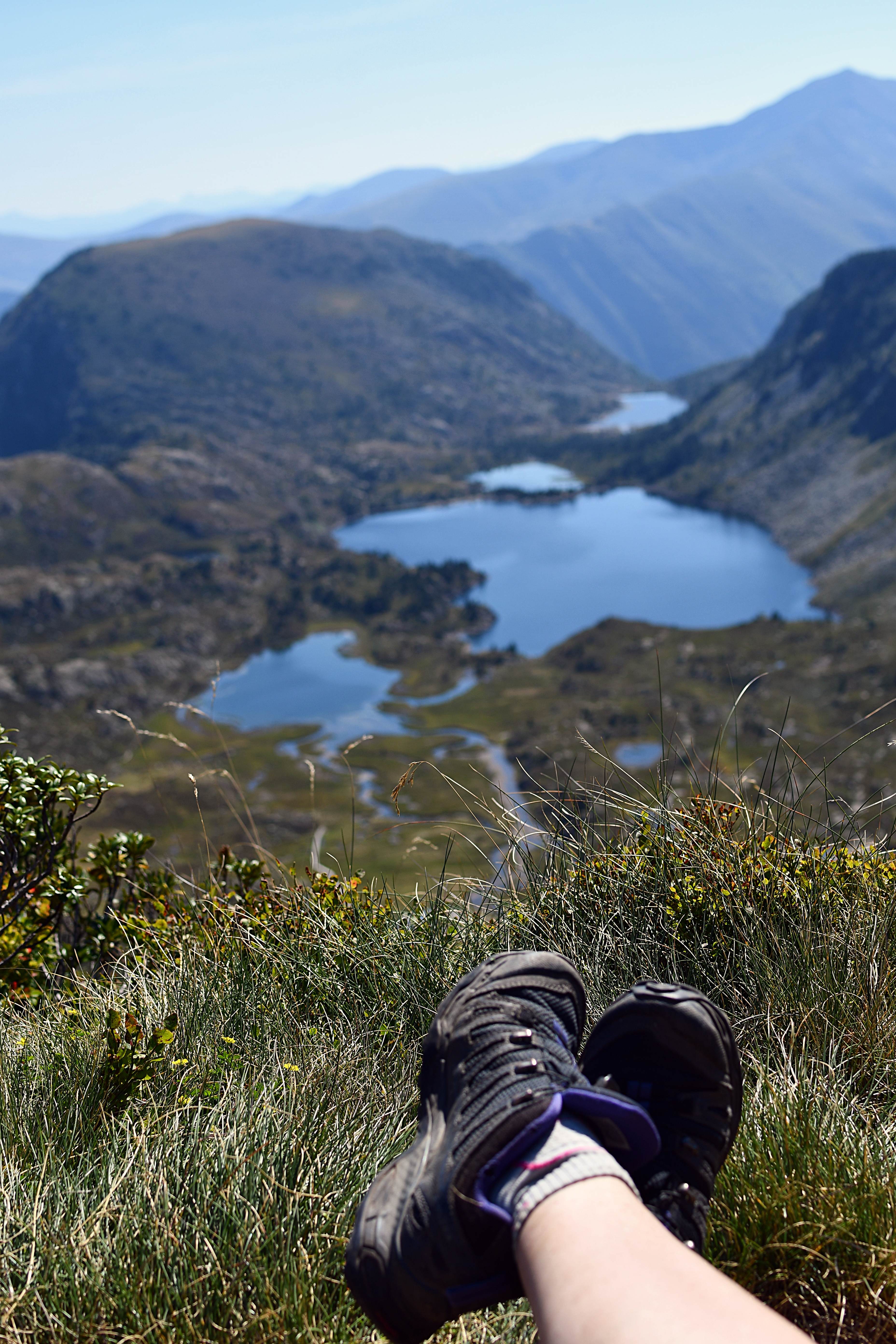 Des pieds dans des chaussures de rando au premier plan, derrière en contre bas, des étangs entourés de montagnes
