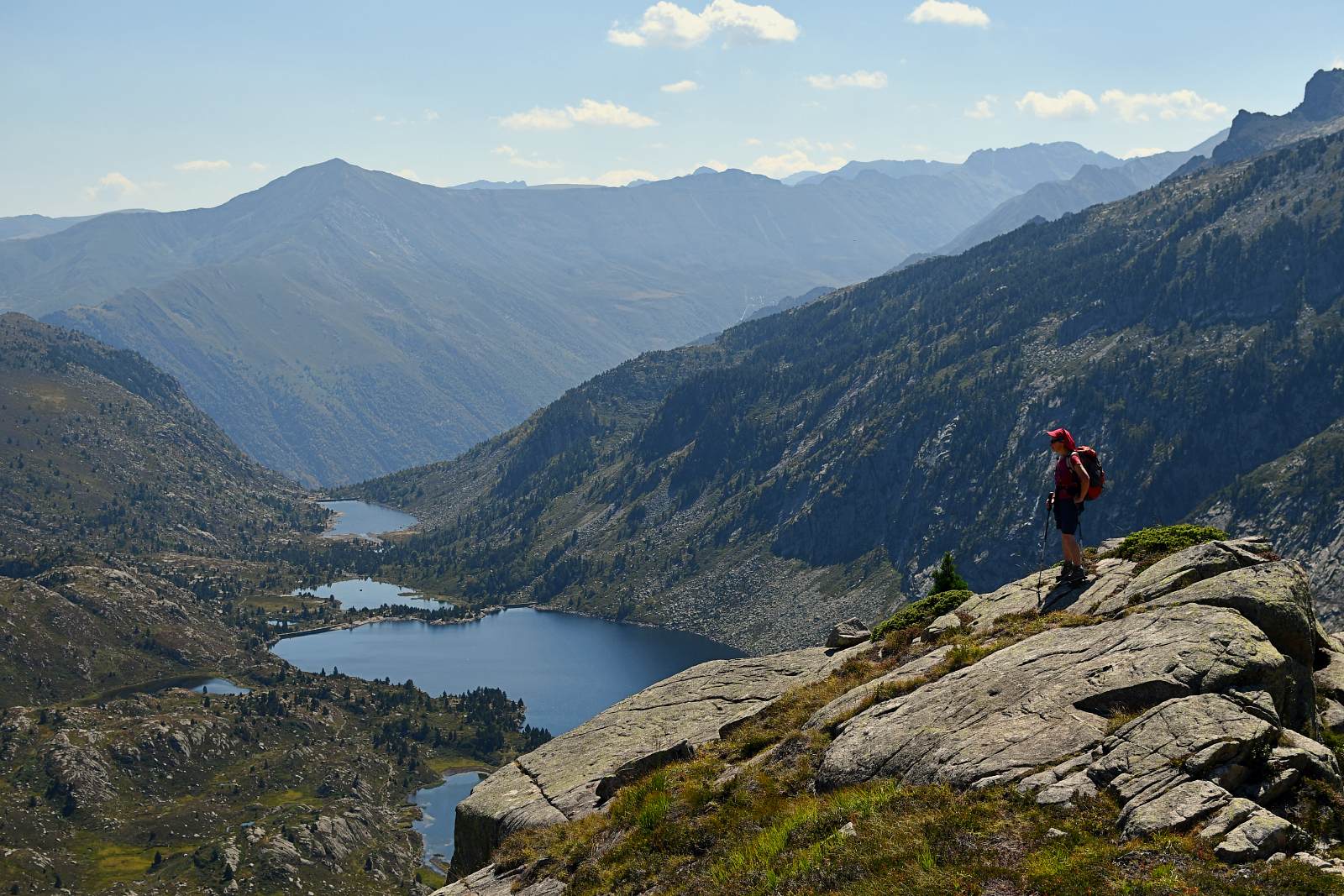 Une randonneuse sur un gros rocher regarde des étangs de montagne en contrebas