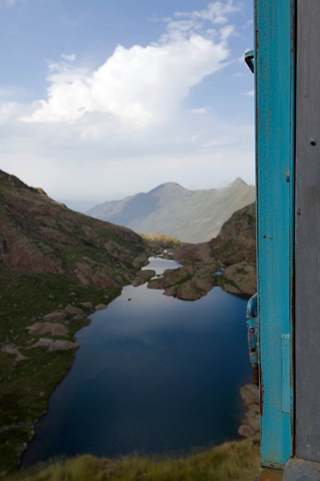 Depuis une fenêtre, vue plongeante sur un étang de montagne
