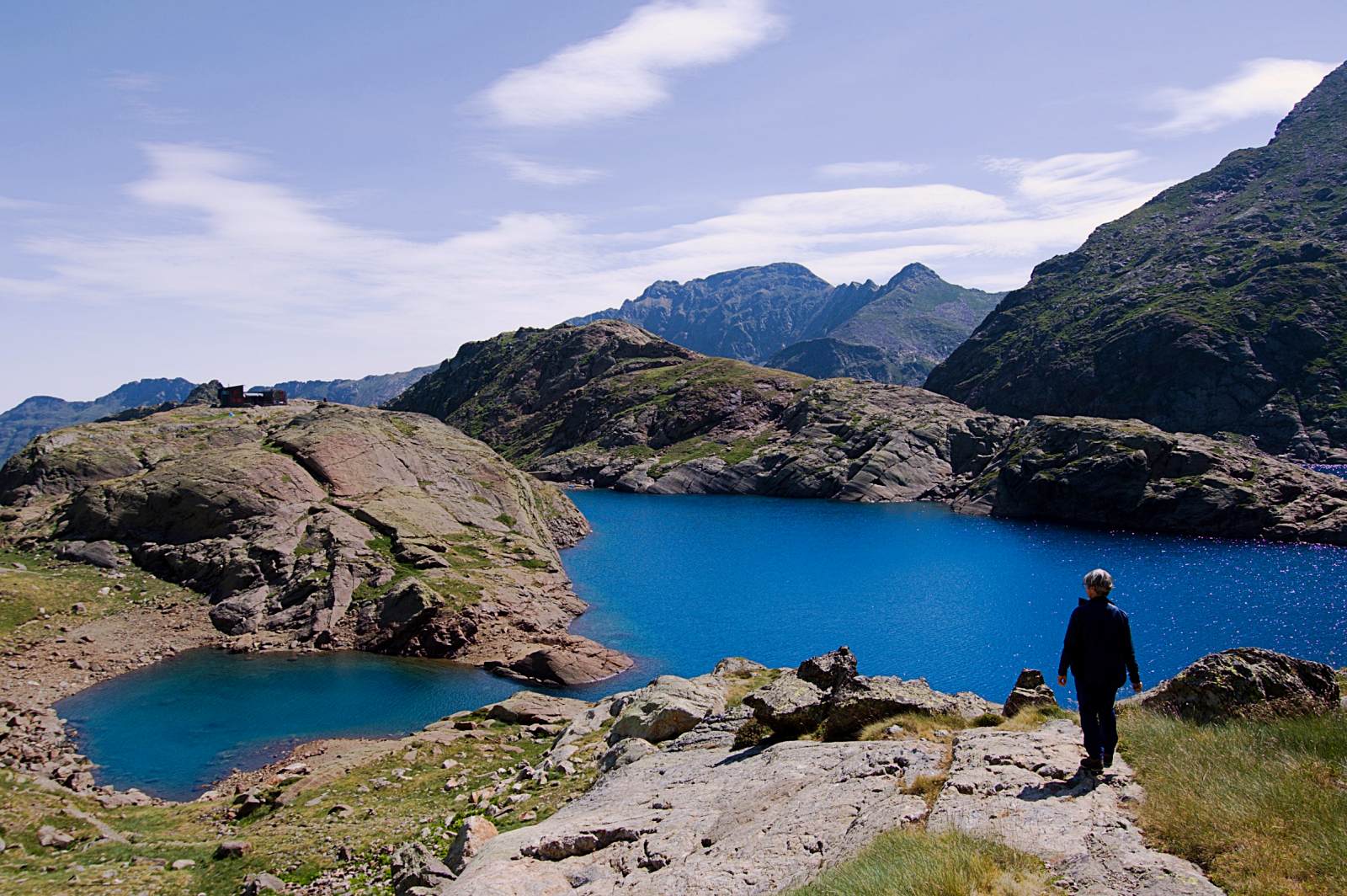 Une femme marche au dessus d'un étang de montagne entouré de roche